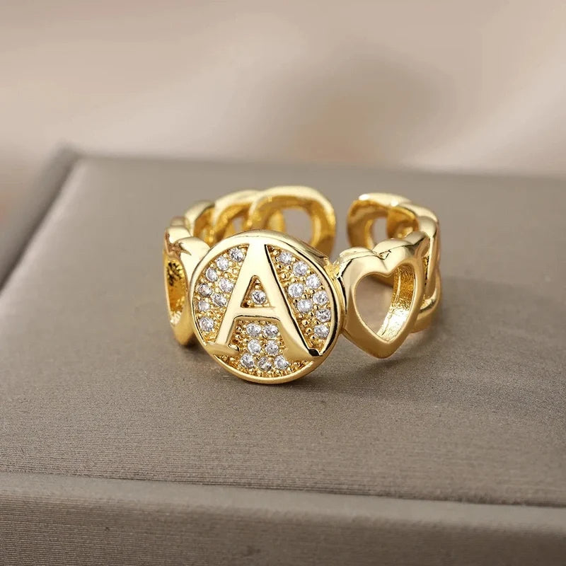 Ring mit Buchstabe in Gold zwischen zwei Herzen