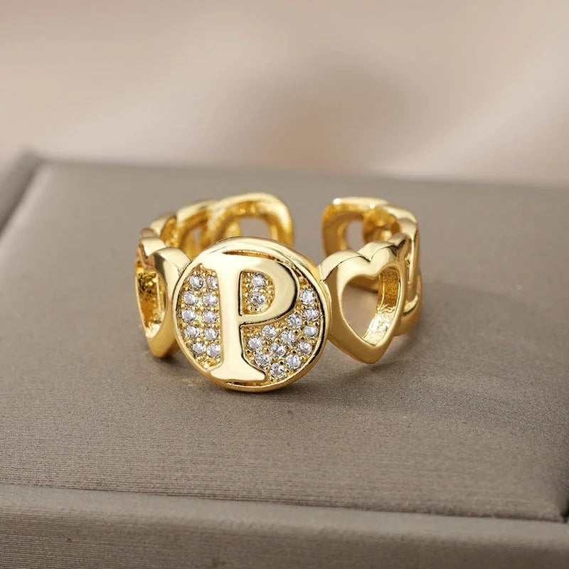 Ring mit Buchstabe in Gold zwischen zwei Herzen