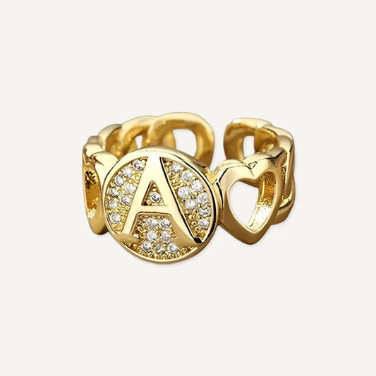 Ring mit Buchstabe in Gold zwischen zwei Herzen